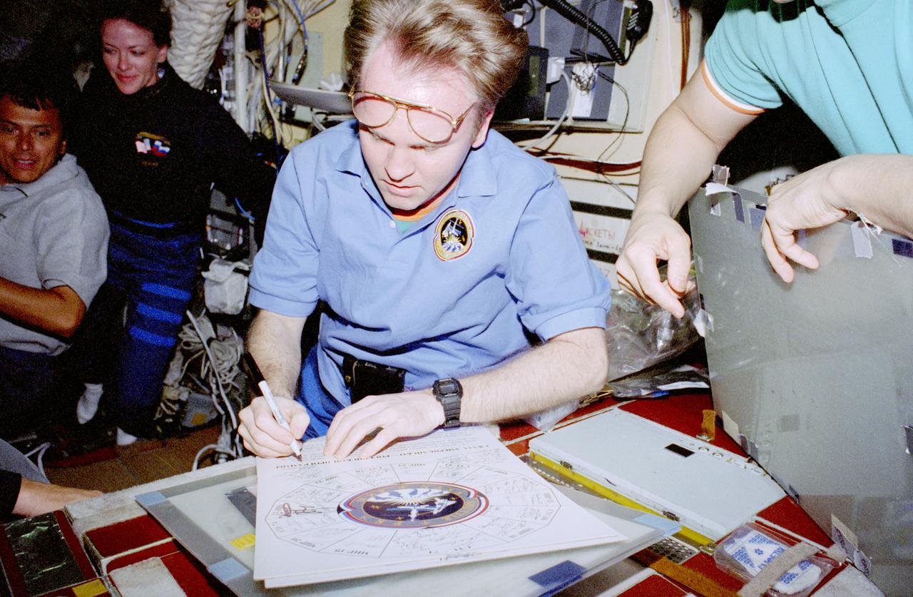 STS091-361-034 (2-12 June 1998) --- Andrew S.W. Thomas signs a plaque containing the names of all the visitors to Russia's Mir space station.  Thomas is the final of seven NASA astronauts to serve as a guest cosmonaut researcher aboard Mir as part of International Space Station (ISS) Phase I.  Looking on in the background are astronauts Franklin R. Chang-Diaz, payload commander; and Janet L. Kavandi, mission specialist.