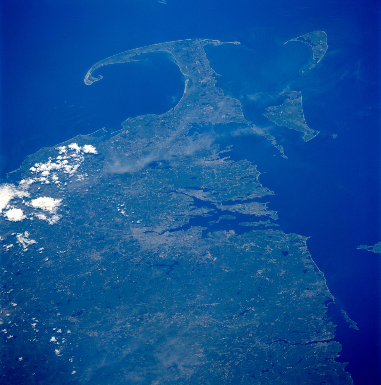 STS091-718-037 (2-12 June 1998)--- This photo taken from the aft flight deck of the Earth-orbiting Space Shuttle Discovery features Cape Cod, an easily recognizable hook-shaped peninsula in southeastern Massachusetts. Sandy and of glacial origin, it extends 65 miles (105 km) into the Atlantic Ocean, has a  varying breadth of 1 to 20 miles (1.6-32 km), and is bounded by Cape Cod Bay (north and west), Buzzards Bay (west), and Vineyard and Nantucket sounds (south). The northern hook of the cape (embracing a recreation area of dunes, marshes, lakes, and pinewoods) was designated the Cape Cod National Seashore (area 68 square miles [176 square km]) in 1961. The Cape Cod Canal cuts across the base of the peninsula shortening the shipping distance between New York City and Boston by more than 75 miles (120 km) and forms part of the Atlantic Intracoastal Waterway.   Cape Cod was named by Bartholomew Gosnold, an English explorer who visited its shores in 1602 and took aboard a &quot;great store of codfish.&quot; In 1620 the Pilgrims landed at the site of Provincetown, on the hooked tip of Cape Cod, before proceeding to Plymouth.
