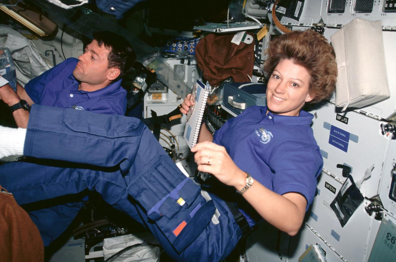 STS093-309-027 (23-27 July 1999) ---  Astronauts Eileen M. Collins, mission commander; and Jeffrey S. Ashby, pilot,  peruse checklists on Columbia's middeck.  Collins and Ashby were joined by three mission specialists for almost five days in Earth orbit.  The busiest of those days was the first, during which they  released into space the world's most powerful X-Ray telescope and initiated a number of in-cabin experiments.