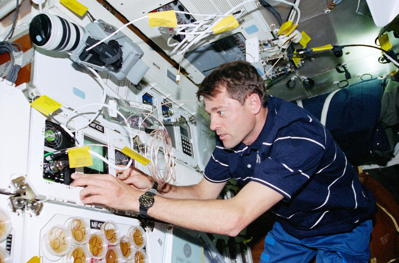STS093-319-029 (23-27 July 1999) ---  Astronaut Jeffrey S. Ashby, pilot,  works with the Space Tissue Loss-B  experiment on Columbia's middeck.    The experiment is set up to observe cells in culture with a video microscope imaging system to record near-real-time  interactions of detecting and inducing cellular responses (macromorphological  changes).