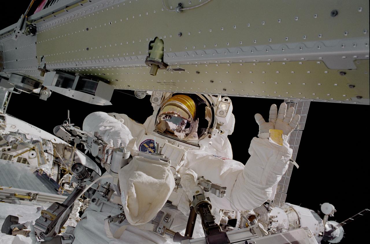 STS097-376-009 (7 December 2000) --- Astronaut Carlos I. Noriega, mission specialist, during the final of the three space walks scheduled for the STS-97 mission to the International Space Station (ISS), waves to his fellow space walker, astronaut Joseph R. Tanner, mission specialist. A small reflection of Tanner can be seen in the helmet as he captures this 35mm image.