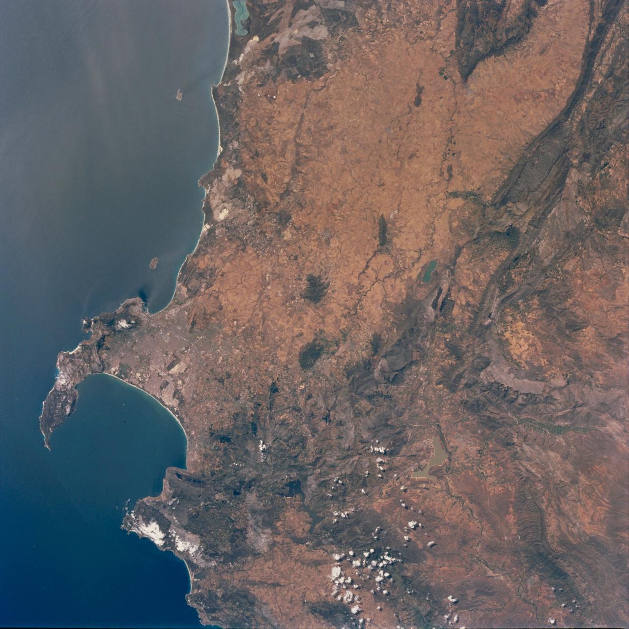 STS097-711-069 (30 Nov. - 11 Dec. 2000) This view featuring Cape Town and the Western Cape Province in the Republic of South Africa was provided by one of the STS-97 astronauts using a 70mm handheld camera aboard the Earth-orbiting Space Shuttle Endeavour. The capital and largest city of Western Cape Province, Cape Town (1995 population in the urban and suburban area  shows in excess of 1.9 million), is visible between False Bay (large, U-shaped bay) and a smaller bay along the Atlantic coast of the peninsula. Within the urban built-up area some of the infrastructure  of Cape Town, including the city center and the harbor and waterfront facilities, can be identified near the small bay (middle left edge of the image). Table Mountain elevation of 3563 feet (1086 meters above sea level) separates the city center (north of the mountain) from the southern suburbs of Cape Town. The Cape of Good Hope, long famous as the gateway from the Atlantic Ocean to the Indian Ocean, is located at the southern tip of the claw-shaped peninsula. False Bay is a popular recreational region for the local residents of the greater Cape Town region, as well as a tourist attraction for people who live beyond the borders of South Africa. The lighter-colored terrain, mainly north of Cape Town, shows a landscape of large, cultivated field patterns. These coastal plains are separated from the interior by a chain of folded mountain ranges that include the Cedarberg (dark, linear,  north/south aligned feature in the upper right corner) and the more complex, folded Herrivierberge Mountains (dark structure, right middle) that are located northeast of Cape Town.