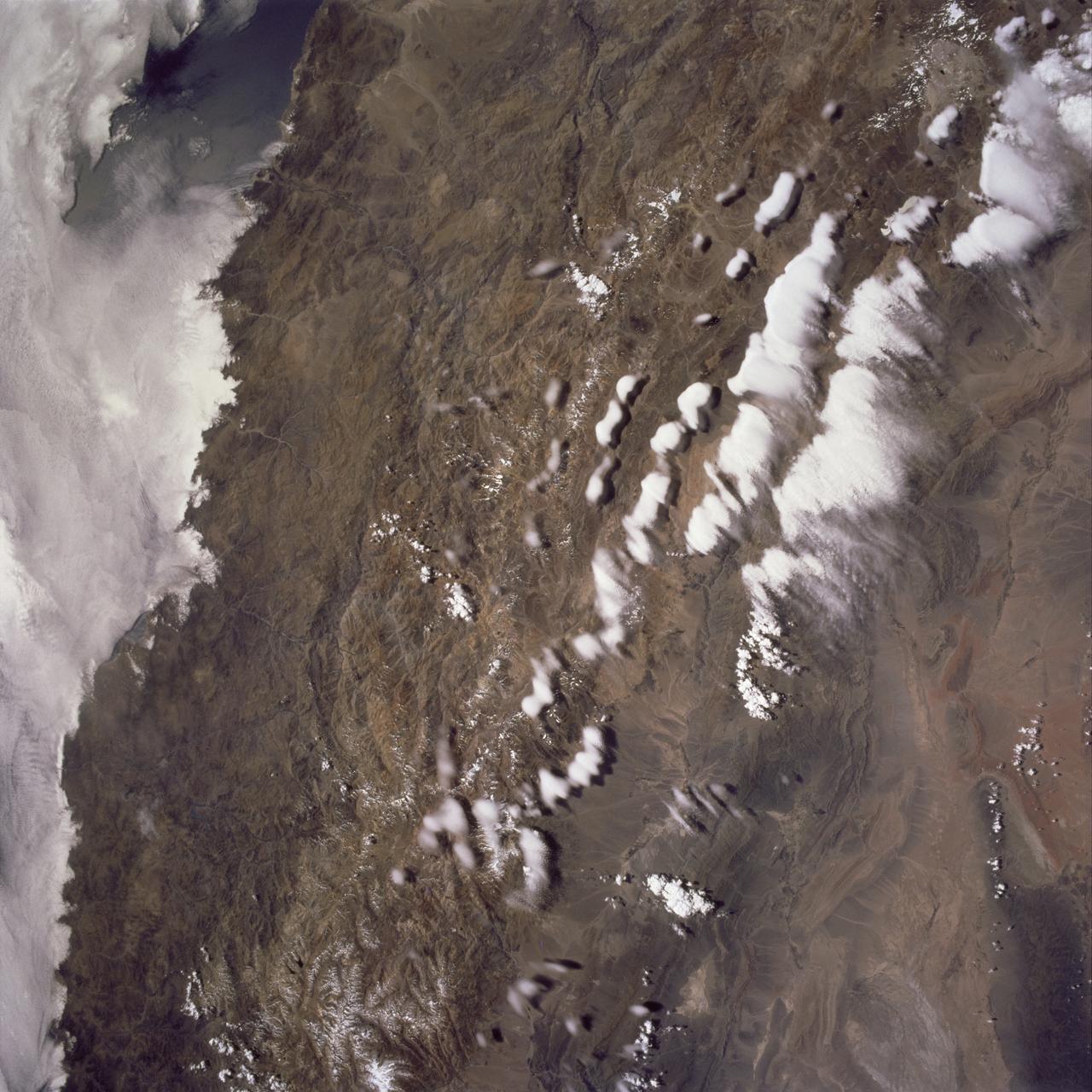 STS097-715-061 (10 December 2000) This view over the Central Andes Mountains in Argentina and Chile was taken on December 10, 2000 by one of the astronauts aboard the Earth-orbiting Space Shuttle Endeavour. Extending 5500 miles (8850 kilometers) along the western coast of South America from northern Colombia to Cape Horn in southern Chile, the Andes are the longest mountain range, above sea level, and the second highest range in the world. According to NASA scientists studying the STS-97 photo collection, this immense system came into existence nearly 70 million years ago. With numerous active volcanoes and a slow uplift, the building of the Andes Mountains continues today rising four inches (10 centimeters) per century, the scientists say. In this north-looking view, snow covers the higher peaks of the range, some of which rise to over 20000 feet (6100 meters) above sea level. Along the left or western portion of the view, clouds can be seen along coastal areas of Chile. In the bottom left quadrant of the scene, the blue waters of the Paloma Reservoir, a recreational lake, are visible. The folded Tontal Range (bottom center) and the Valle Fertil Range (upper right quadrant and partially cloud covered) of western Argentina can be seen. The rocks of these ranges, the scientists point out, are ancient compared to the younger volcanic peaks and ranges of the Andes. The city of San Juan, Argentina is visible on the eastern (right) base of the Tontal Range in the lower right quadrant of the view.