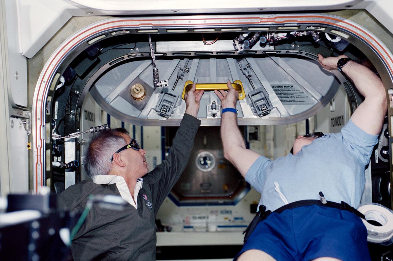STS098-352-0025 (11 February 2001) --- STS-98 mission commander Kenneth D. Cockrell (left) assists as Expedition One commander William M. (Bill) Shepherd opens the hatch to the newly attached Destiny laboratory. The crews of Atlantis and the International Space Station entered the laboratory shortly after this photo was made on February 11; and the astronauts and cosmonauts spent the first full day of what are planned to be years of work ahead inside the orbiting science and command center. Members of both crews went to work quickly inside the new module, activating air systems, fire extinguishers, alarm systems, computers and internal communications. The crew also continued equipment transfers from the shuttle to the station.