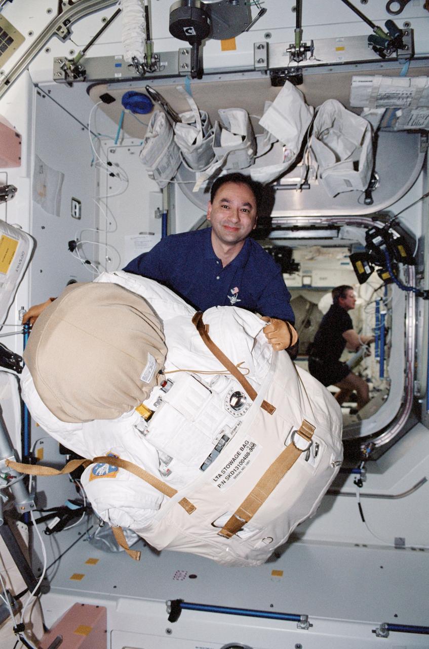 STS098-361-016 (7-20 February 2001) --- Astronaut Mark L. Polansky, STS-98 pilot, moves one of the Extravehicular Mobility Unit (EMU) space suits in its storage bag onboard the International Space Station (ISS). William M. (Bill) Shepherd, Expedition One mission commander, can be seen as he works in the background.