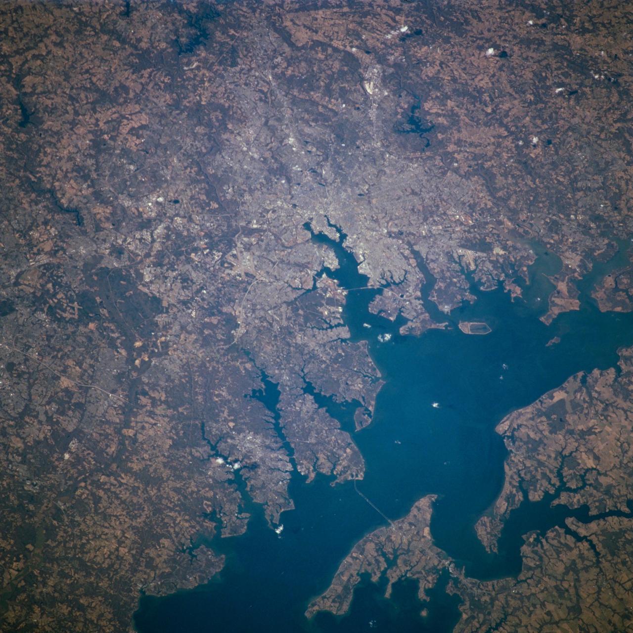 STS098-716-057 (7-20 February 2001) --- Baltimore, Maryland can be identified in this northwest-looking view, photographed with a 70mm handheld camera from the Space Shuttle Atlantis, which shows the western shore of Chesapeake Bay. Numerous drowned river valleys provide excellent natural harbors along the periphery of the bay. Baltimore’s harbor has been developed along one of these drowned valleys, the Patapsco River. With a population of over 2.5 million people, the greater Baltimore urban area is part of the northeastern U.S. Megalopolis that extends from the Boston (MA) area to Richmond (VA). Specific features that can be seen in the image include a short segment of Interstate Highway 95 that connects southwest Baltimore with northeast Washington, D.C.; the intersecting runways of Baltimore-Washington International Airport south of downtown Baltimore; Francis Scott Key Bridge that skirts around the southeast side of Baltimore; the Chesapeake Bay Bridge that spans the bay and connects the Baltimore area with the eastern shore of Maryland; and the central business district of Baltimore where the two arms of the inner harbor terminate. The darker-looking vegetation cover is mixed hardwood forests (notice that many wooded areas are located along streambeds and floodplains of small river valleys), while lighter-looking land parcels in the rural countryside is used for crops or pasturelands.