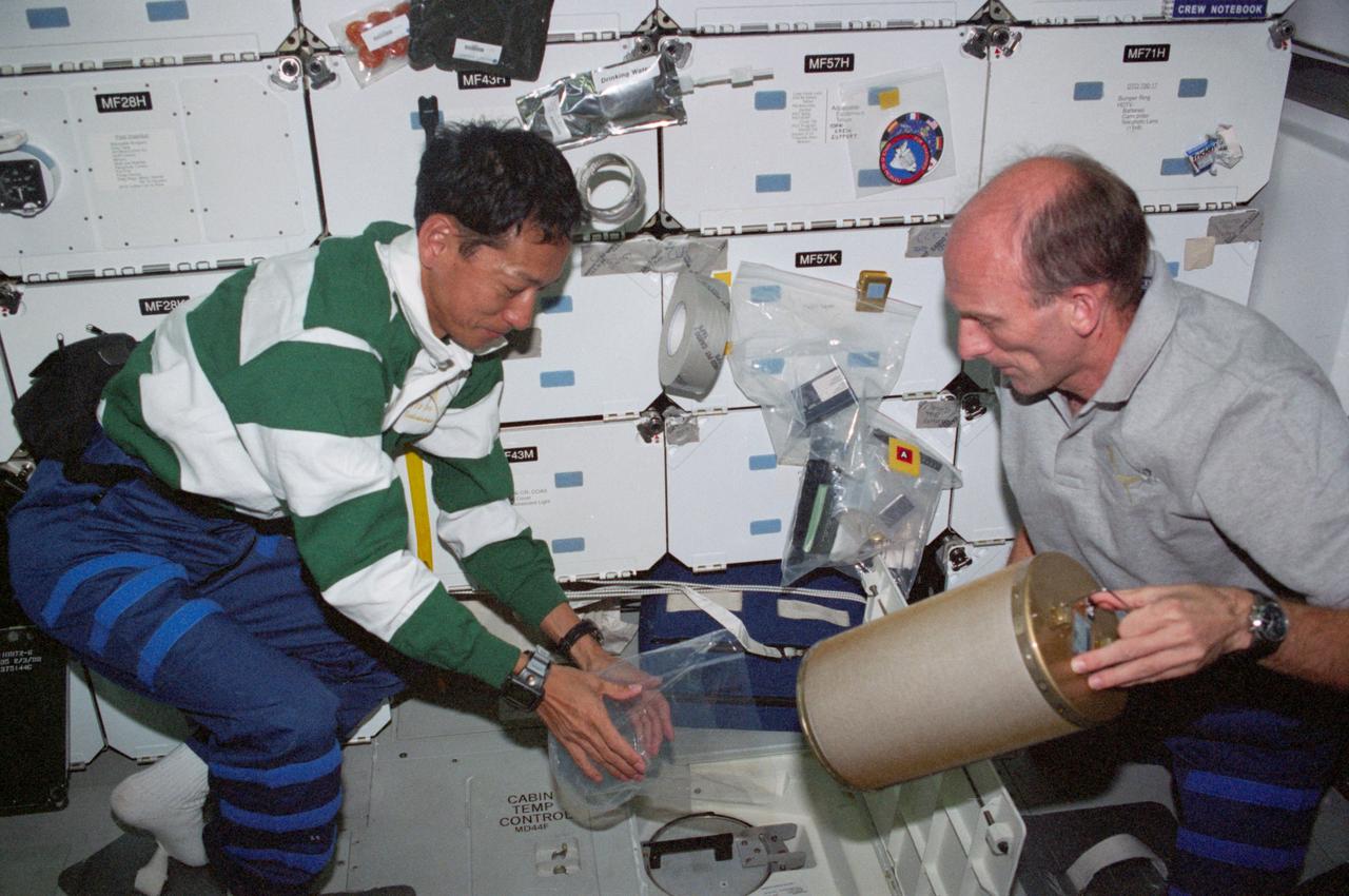 STS099-311-026 (11-22 February 2000) ---Astronauts Mamoru Mohri (left) and Gerhard P. J. Thiele, both mission specialists, change out lithium hydroxide canisters on the middeck of the Earth-orbiting Space Shuttle Endeavour. Mohri represents Japan?s National Space Development Agency (NASDA) and Thiele represents the European Space Agency (ESA).