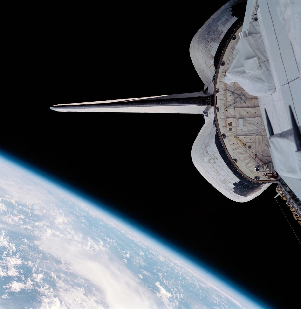 STS099-703-082 (11-22 February 2000) --- Part of the Space Shuttle Endeavour's aft cargo bay, its vertical stabilizer and orbital maneuvering system (OMS) pods are seen in this 70mm frame. Part of Earth's horizon, with an expanse of  heavy cloud cover over land and water, is at bottom of frame.