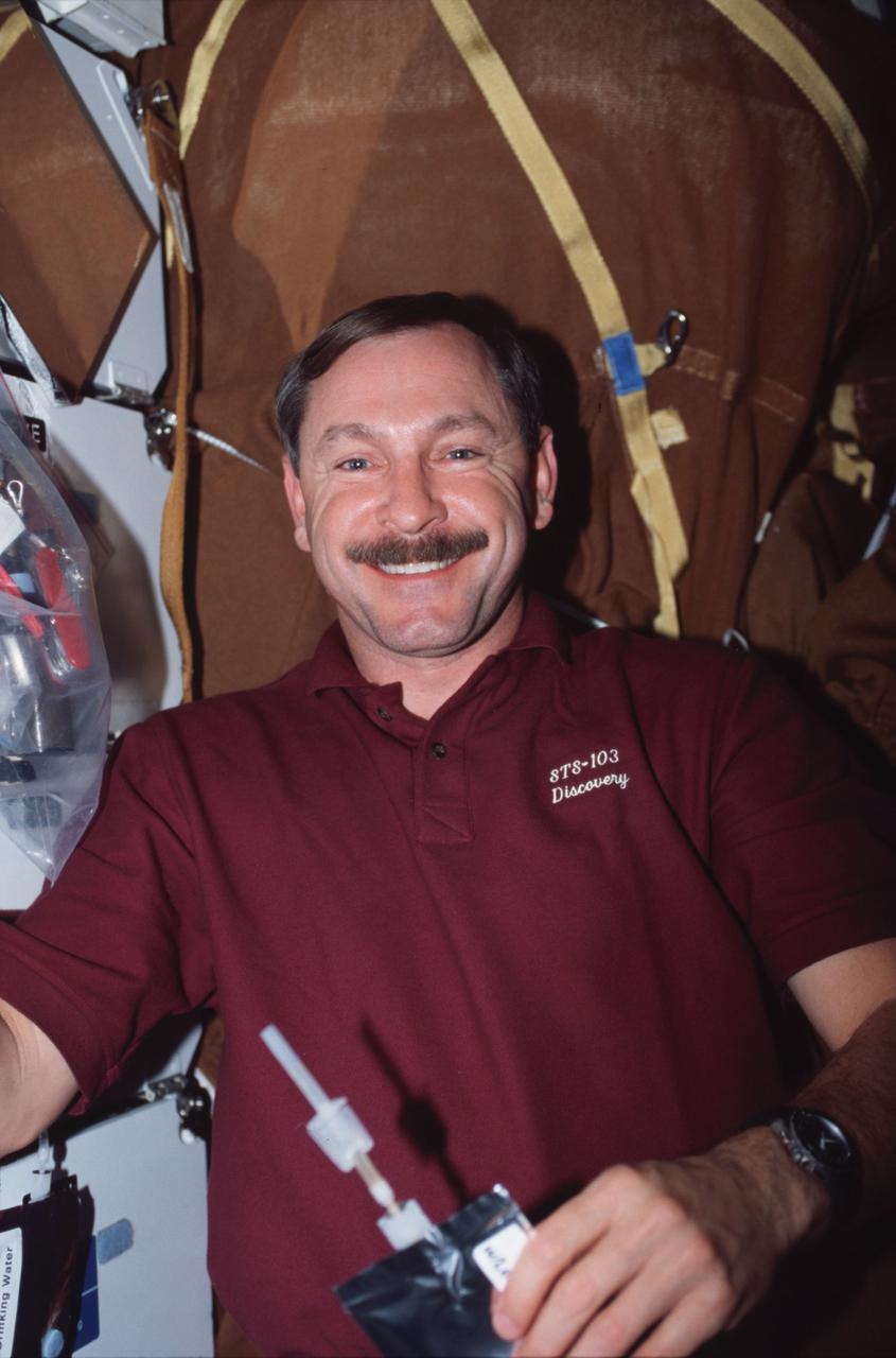 STS103-329-018 (19-27 December 1999) --- Astronaut Curtis L. Brown Jr., mission commander, on Discovery's mid deck holding a drink bag.