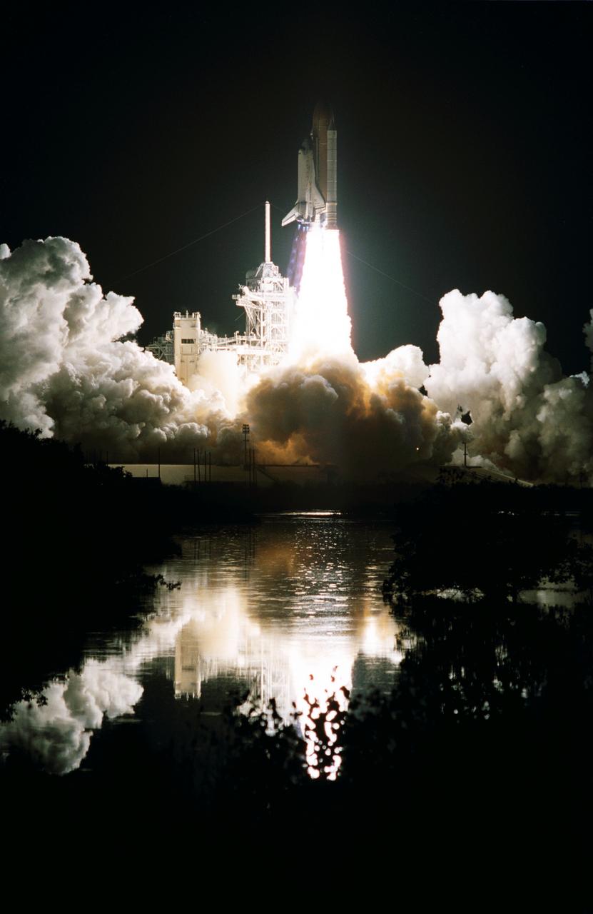 STS103-S-006 (19 December 1999) --- The Space Shuttle Discovery, reflected in nearby water, lifts off into the clear night sky to begin the 96th mission in the STS program.   Liftoff occurred at 7:50 p.m. (EST), December 19, 1999, from Launch Pad 39B.  Onboard were astronauts Curtis L. Brown, Jr., Scott J. Kelly, Steven L. Smith, C. Michael Foale, John M. Grunsfeld, Claude Nicollier and Jean-Francois Clervoy. Switzerland's Nicollier and France's Clervoy represent the European Space Agency (ESA).