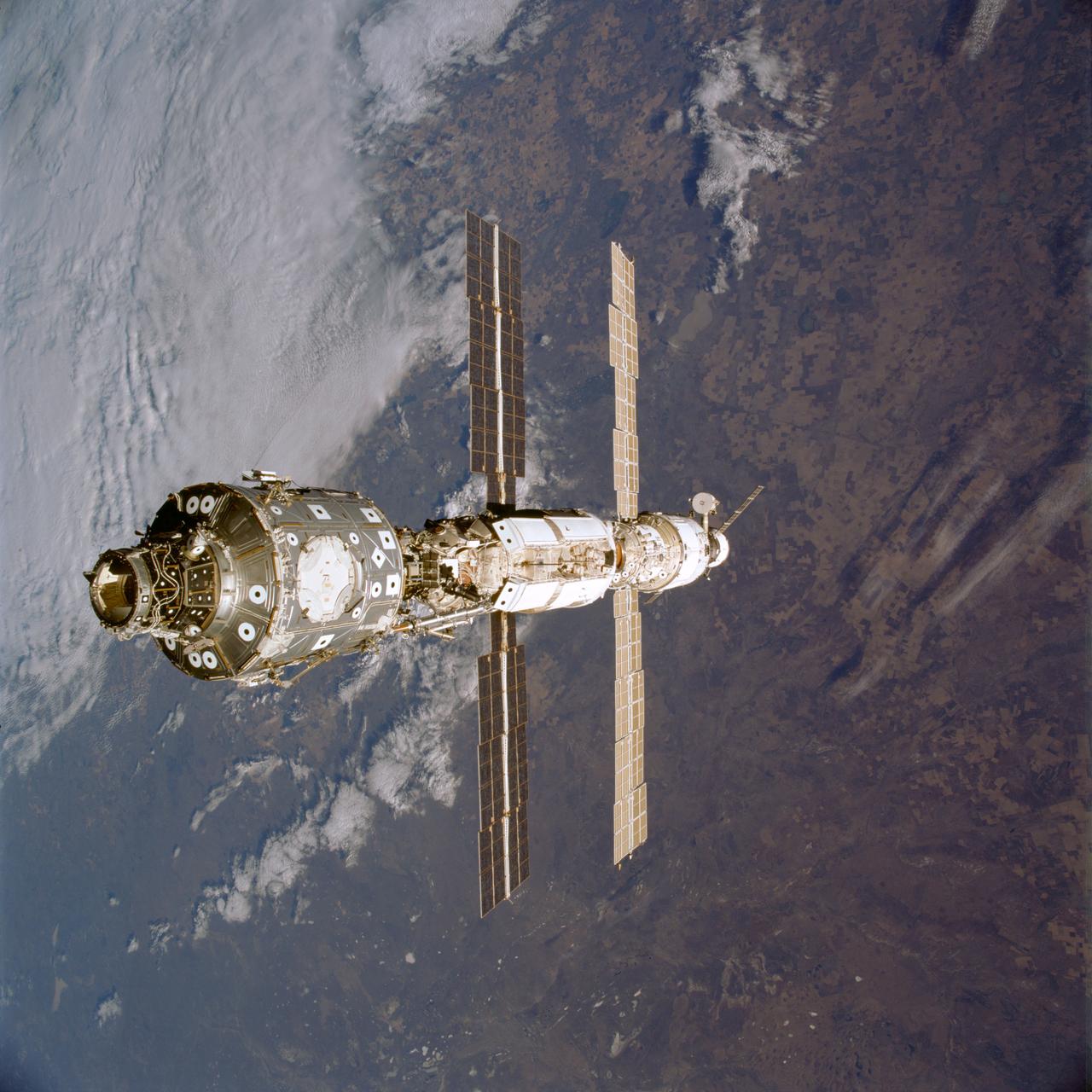STS106-709-026 (8-20 September 2000) --- The STS-106 crew members used a  70mm handheld camera to capture this  view of the International Space Station (ISS) over a moderately cloud-covered  land area. The station component nearest the camera is the U.S.-built Unity node,  which is connected with the Russian-built Functional Cargo Block (FGB) or Zarya.  The FGB was linked in July with the Service Module or Zvezda,  seen near the bottom of ISS in this angle.  On the far end, next to the service module, is the Progress supply ship, which joined ISS in August.