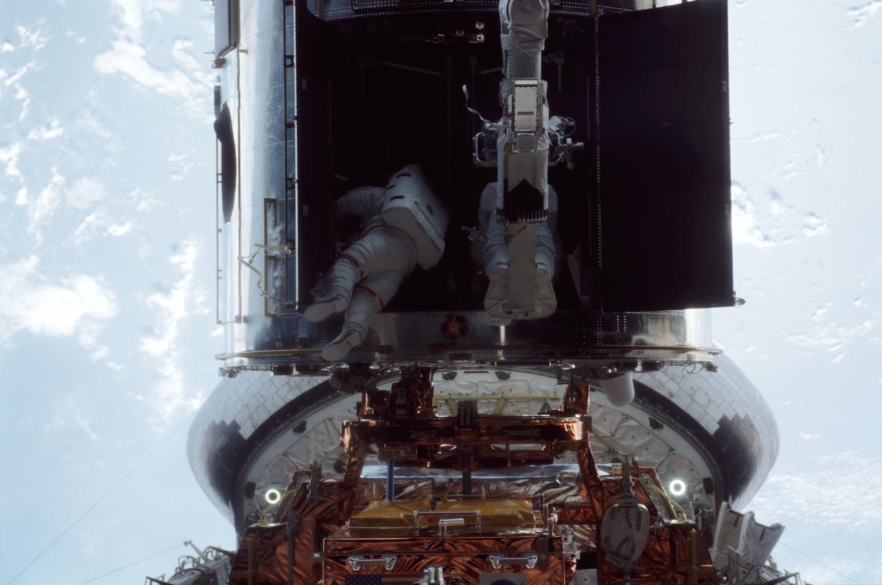 STS109-315-005 (8 March 2002) --- Barely visible within the Hubble Space Telescope's heavily shadowed shroud doors, astronauts John M. Grunsfeld (left) and Richard M. Linnehan participate in the final space walk of the STS-109 mission. The crew of the space shuttle Columbia completed the last of its five ambitious space walks early on March 8, 2002, with the successful installation of an experimental cooling system for Hubble&#0146;s Near-Infrared Camera and Multi-Object Spectrometer (NICMOS). The NICMOS has been dormant since January 1999 when its original coolant ran out.  Astronauts  Grunsfeld and Linnehan began their third spacewalk of the mission at 2:46 a.m. CST. Linnehan was given a ride on the shuttle&#0146;s robotic arm to the aft shroud doors by astronaut Nancy J. Currie, working from the aft flight deck of Columbia. After the shroud doors were open, Linnehan was moved back to Columbia&#0146;s payload bay to remove the NICMOS cryocooler from its carrier. Grunsfeld and Linnehan then installed the cryocooler inside the aft shroud and connected cables from its Electronics Support Module (ESM). That module was installed on March 7 during a spacewalk by astronauts James H. Newman and Michael J. Massimino.