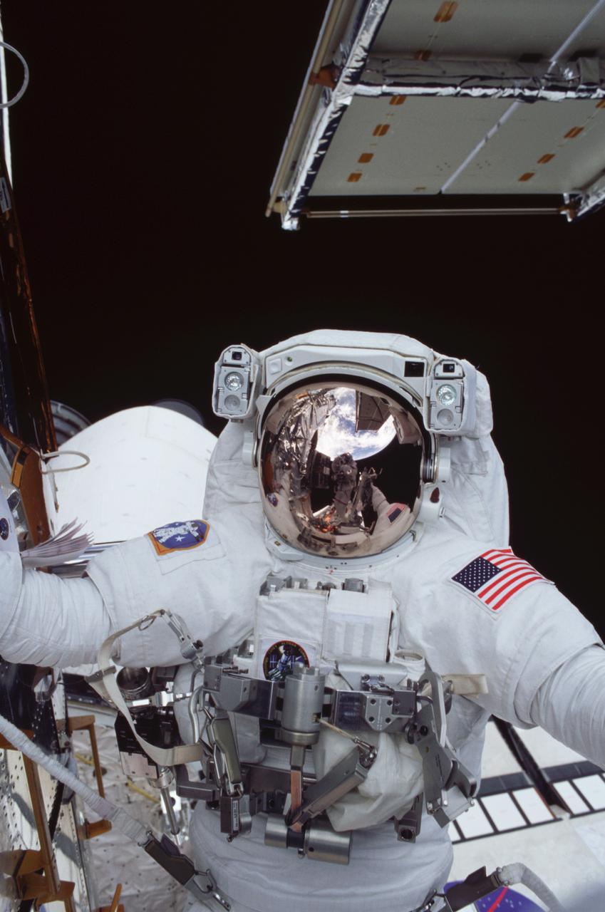 STS109-322-028 (6 March 2002) --- Astronaut Richard M. Linnehan, STS-109 mission specialist, participates in the third of five space walks to perform work on the Hubble Space Telescope (HST). Linnehan's sun shield reflects   astronaut John M. Grunsfeld and    the blue and white Earth's hemisphere as well as one of the telescope's new solar arrays. The third overall STS-109 extravehicular activity (EVA) marked the second of three for Linnehan and Grunsfeld, payload commander.  On this particular walk, the two turned off the telescope in order to replace the power control unit or PCU--the heart of its power system.  Grunsfeld took this photo with a 35mm camera.