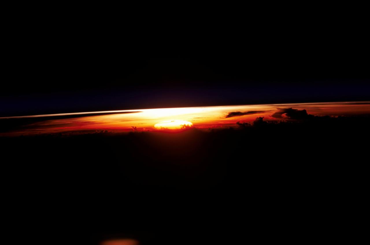 STS109-345-032 (1-12 March 2002) --- One of the astronauts aboard the Space Shuttle Columbia photographed this west-looking view featuring the profile of the atmosphere and the setting sun.  The shuttle was located over the Java Sea to the south of Kalimantan (Borneo) in Indonesia when this image was acquired.  Visible to the right of the setting sun are cloud tops from some thunderstorms.  The sun's reflection (bright spot over the setting sun) can be seen off the upper layers of the earth's atmosphere.