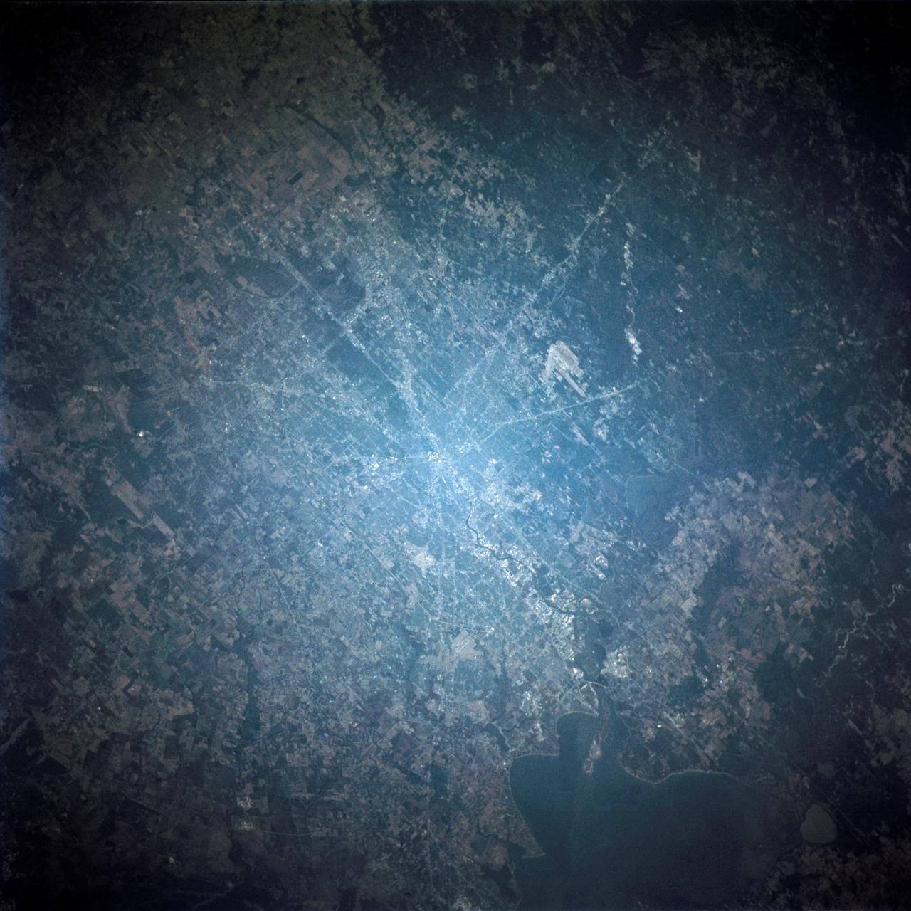 STS109-714-035 (1-12 March 2002) --- The astronauts on board the Space Shuttle Columbia took this 70mm picture featuring the greater metropolitan Houston, Texas area. The view direction is northwest, with Houston's downtown as the brightest region (center) where major highways converge. Interstate 10 is a fine line extending towards the lower right, around the north side of Galveston Bay, part of which appears in the lower right corner. The interstate also appears as a line cutting through the wooded parts of west Houston (just west of downtown). Bush Intercontinental Airport is the largest light patch on the view north of downtown, and lies next to Highway 59, a thin white line that stretches toward the right side of the picture. Forests of East Texas make the top right corner of the view a dark green.