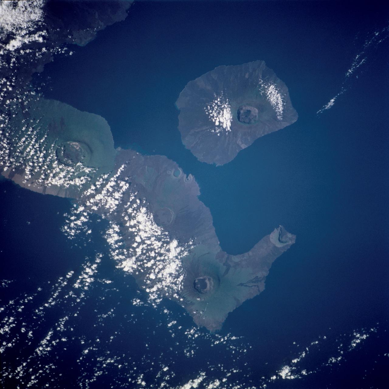 STS109-718-102 (1-12 March 2002) --- The astronauts on board the Space Shuttle Columbia took this 70mm picture featuring the Galapagos Islands. For orientation purposes, north is towards the bottom of the view. Most of the largest island in the Galapagos group, Isla Isabela, stretches across the middle of the frame. The circular feature on this island at bottom is Volcano Wolf (1707 meters in altitude). Volcano Darwin (1280 meters in sea level) is the next volcano above and to the left, partly ringed with cloud. The single island top right is Isla Fernandina, the top of another volcano (1547 meters). Recent lava flows appear as darker surfaces and the older surfaces appear green, as a result of unusual rains and vegetational greening in this normally arid part of the world. The Equator passes exactly through Volcano Wolf, roughly left to right.