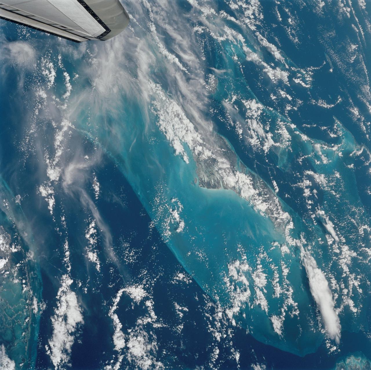 STS112-705-011  (7-18 October 2002) --- The light-blue region in the middle of this view, photographed from the Space Shuttle Atlantis, is the shallow flat platform known as the Great Bahama Bank.  The platform is covered by less than 100 feet of water.  Andros Island, the biggest island in the Bahamas chain, is the highest part of this platform and appears partly under cloud cover in the center of the view.  The edges of the platform are steep, dropping off thousands of feet into the ocean depths, the deepest water indicated  by deep blues. The 50-mile-wide Strait of Florida is the deep water along the left and lower sides of the view.  The Key Largo part of the Florida Peninsula appears in the extreme lower left.