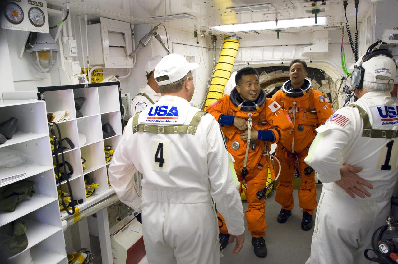 STS119-S-015 (15 March 2009) --- In the White Room on launch pad 39A at NASA's Kennedy Space Center in Florida, Japan Aerospace Exploration Agency astronaut Koichi Wakata (left, facing camera) and NASA astronaut Joseph Acaba, both STS-119 mission specialists, attired in their shuttle launch and entry suits, don their harnesses, which includes a parachute pack, before crawling through the open hatch into Space Shuttle Discovery. The White Room is at the end of the orbiter access arm on the fixed service structure and provides access into the shuttle. Members of the closeout crew assisted the crewmembers. Liftoff is scheduled for 7:43 p.m. (EDT) on March 15, 2009.
